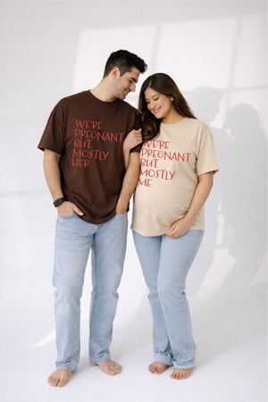 Man and woman wearing matching t-shirts with humorous pregnancy text on a white background